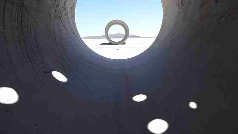 Nancy Holt, Sun Tunnels, 1973-1976 - Lucin, Utah 

Nancy Holt is most widely known for her large-scale artwork Sun Tunnels (located in Lucin, UT); however, she has created works in public places all over the world. The artist's interest in light, perspective, time, and space certainly influenced her photographs, films, sculpture, and installation art, but perhaps it is most magnificently illustrated in her Land art. Land art emerged in the 1960s, coinciding with a growing ecology movement in the United States, which asked people to become more aware of the impact they can have on the natural environment. Land art changed the way people thought of art; not only did it take art out of the gallery and museum, but it also took art out of the market. Many Land art sites are located in remote, uninhabited regions. We are lucky that such an influential work of art is within a day's drive from the UMFA.
 
Sun Tunnels consists of four massive concrete tunnels, each eighteen feet long and nine feet in diameter, laid out in the desert in an open X configuration. On the solstices, the tunnels frame the sun as it passes the horizon at sunrise and sunset. In the top of each tunnel, Holt drilled small holes to form the constellations of Draco, Perseus, Columba, and Capricorn. These holes, and the tunnels themselves, act as frames or lenses through which the visitor can view the surrounding sky and landscape of the Great Basin Desert.
 
To create her 1978 film Sun Tunnels, Holt camped for days on end in the barren desert. In Holt's cinematic and photographic documents currently on view at the Utah Museum of Fine Arts, we can observe myriad nuances of light and shadow inhabiting the installation over time. But to fully experience this important work of Land art, climb into the tunnels, view the surrounding landscape through the cylindrical frames, and feel the desert air in Utah's Great Basin.
 
<a href='http://umfa.utah.edu/suntunnels_selfguide' rel='noreferrer nofollow'><figcaption id=